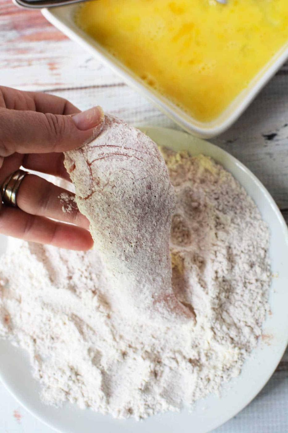 Hand dipping chicken fillet in flour, with beaten eggs nearby, this process mirrors the initial steps of learning how to make chicken tenders.