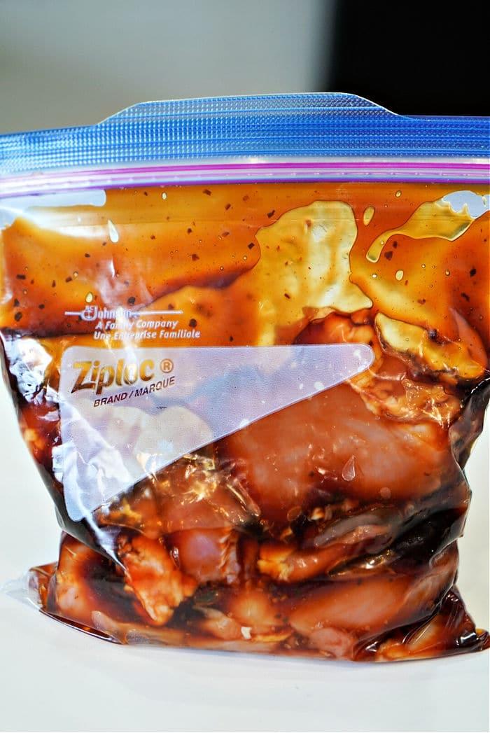 A plastic zip-lock bag filled with marinating chicken in a dark sauce, soon to become delicious baked teriyaki chicken thighs.