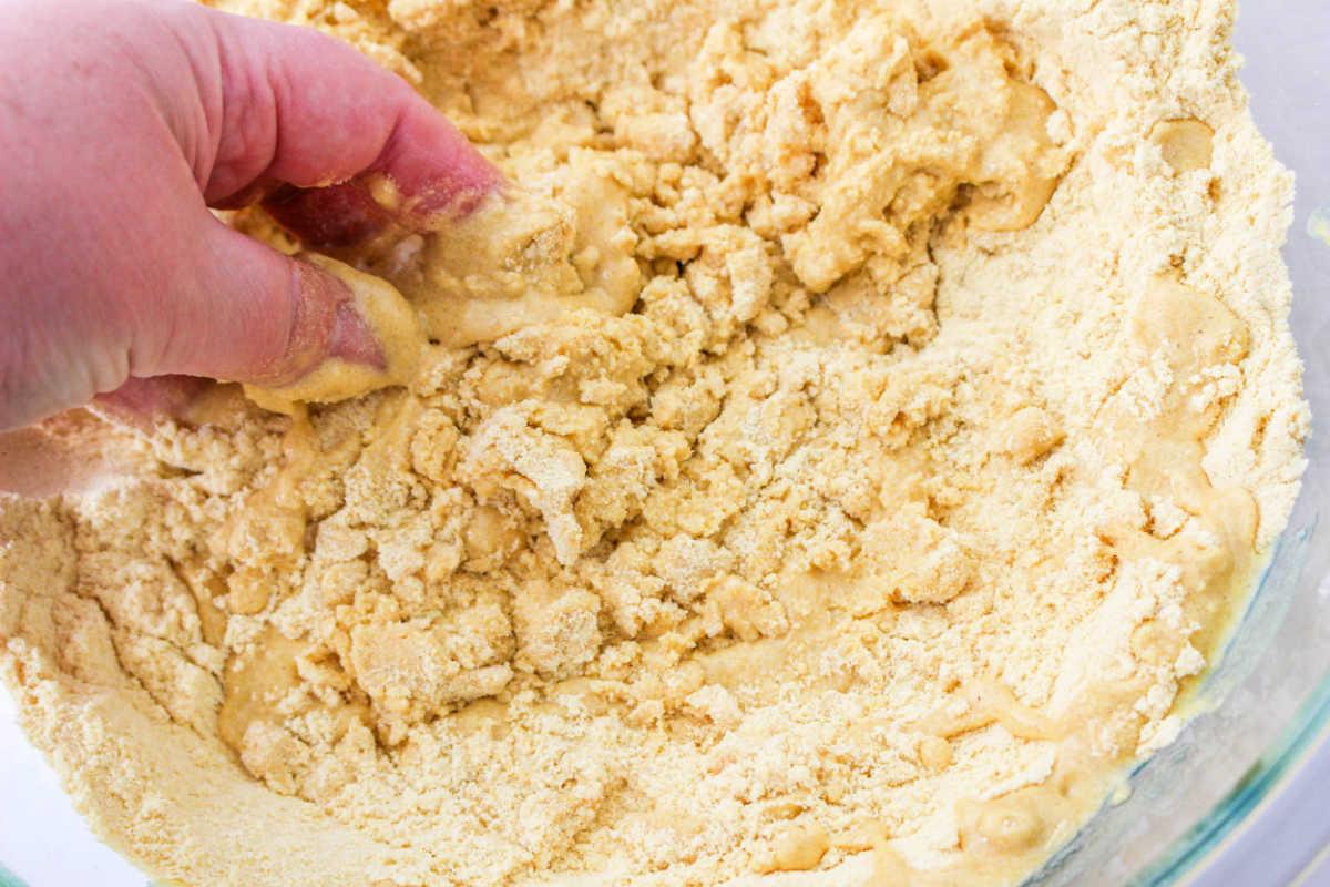 Hand mixing crumbly masa dough in a clear bowl, perfecting the art of how to make tamales masa.