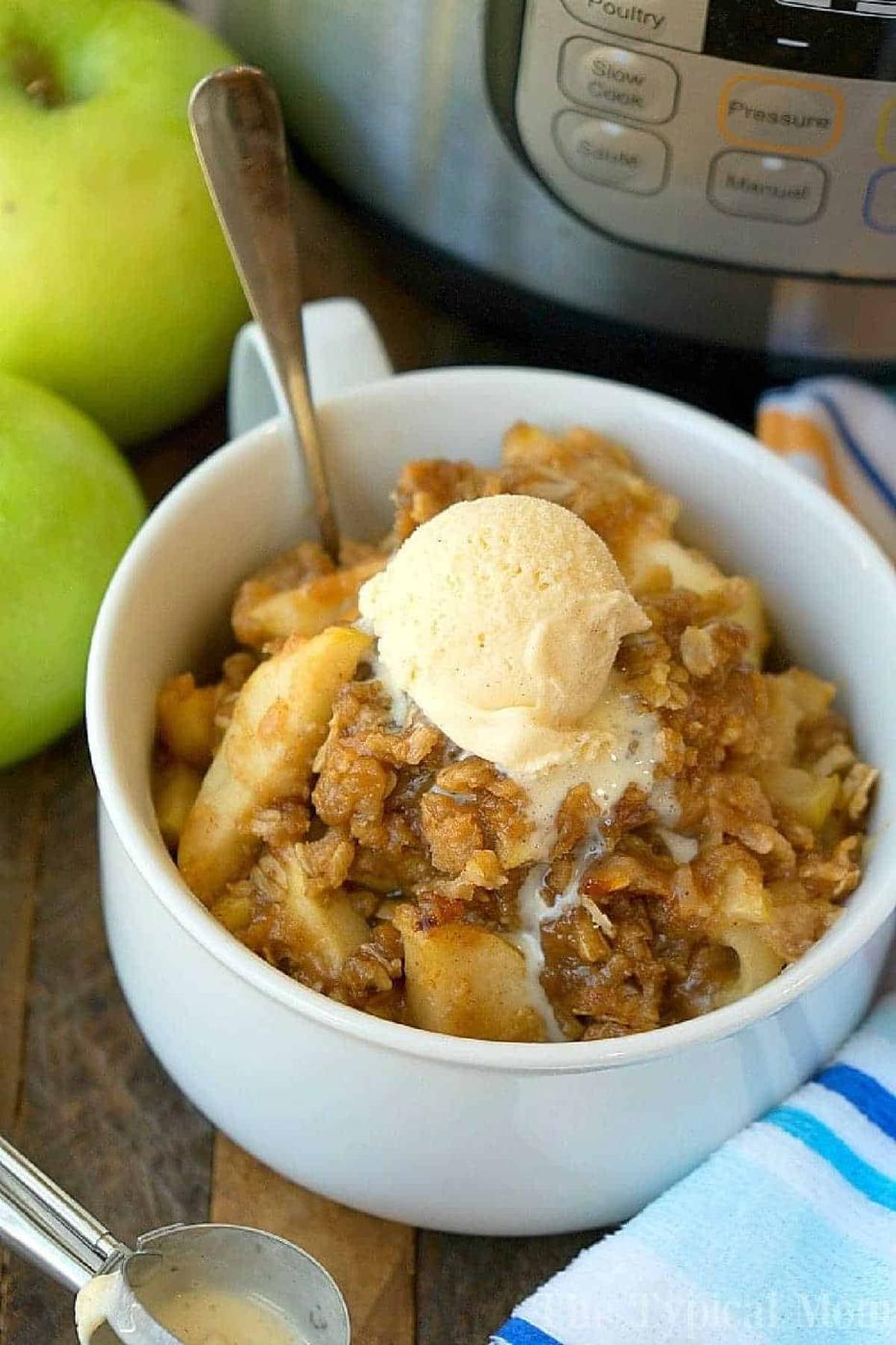 A bowl of instant pot apple crisp topped with vanilla ice cream, with fresh apples and an Instant Pot in the background.
