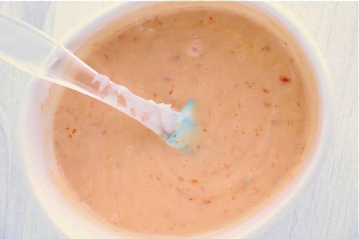 Close-up of a creamy bang bang shrimp sauce with specks, perfect for drizzling over instant pot bang bang shrimp, served in a white bowl with a spoon.