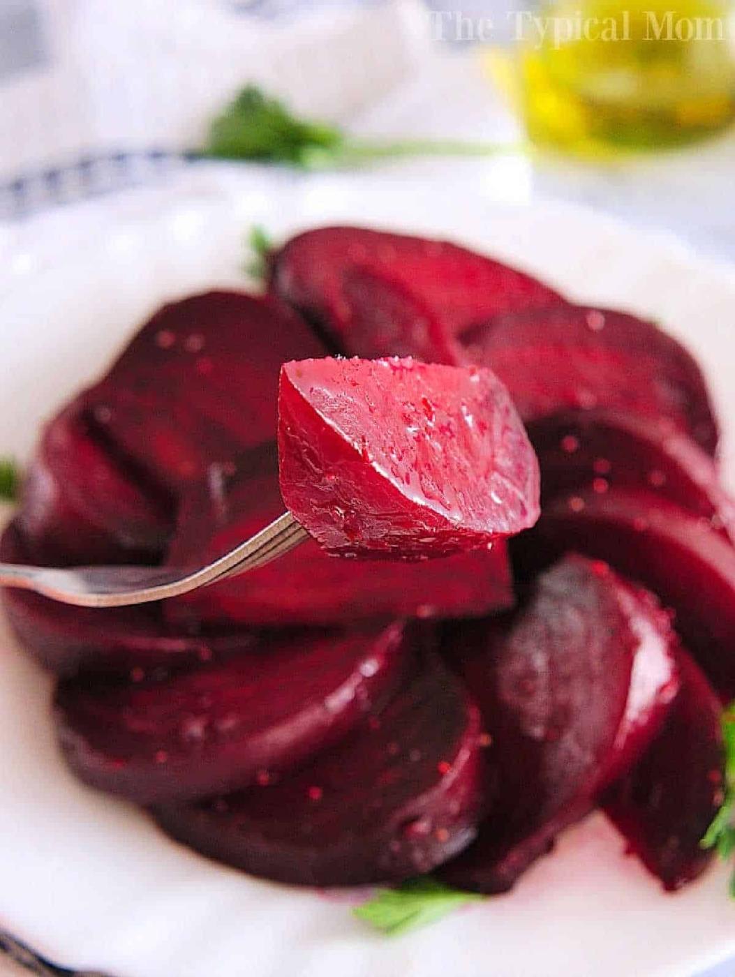 Close-up of a fork holding a slice of cooked beet, tenderly prepared using an Instant Pot, on a plate with more beet slices in the background.