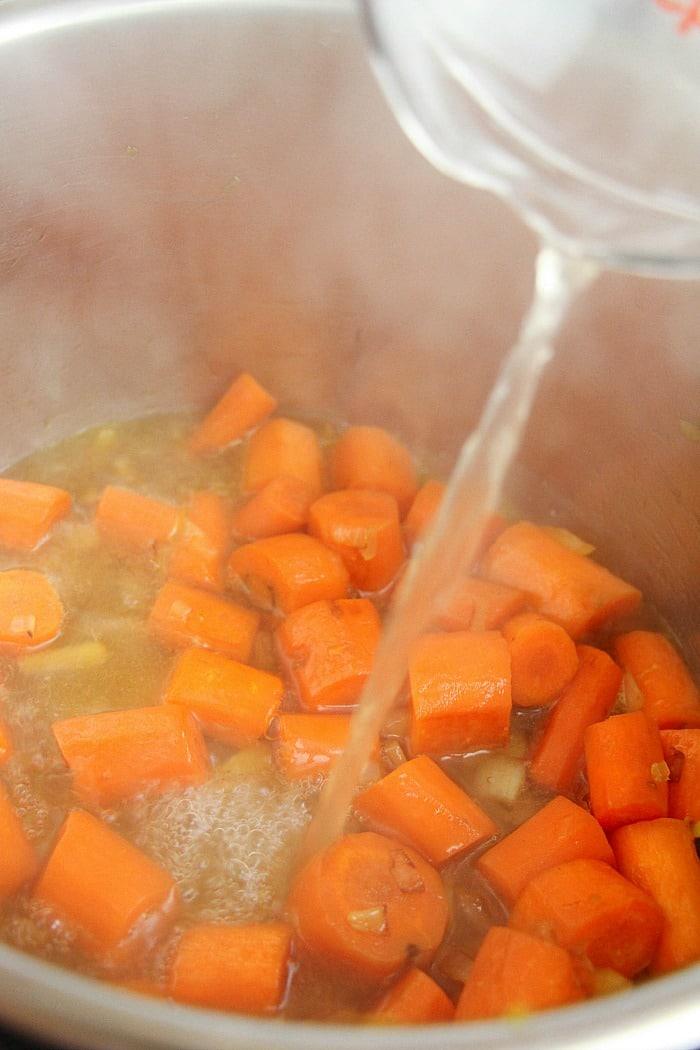 Learn how to cook carrots by watching the water being poured into a pot where chopped carrots simmer gracefully in flavorful broth in instant pot.