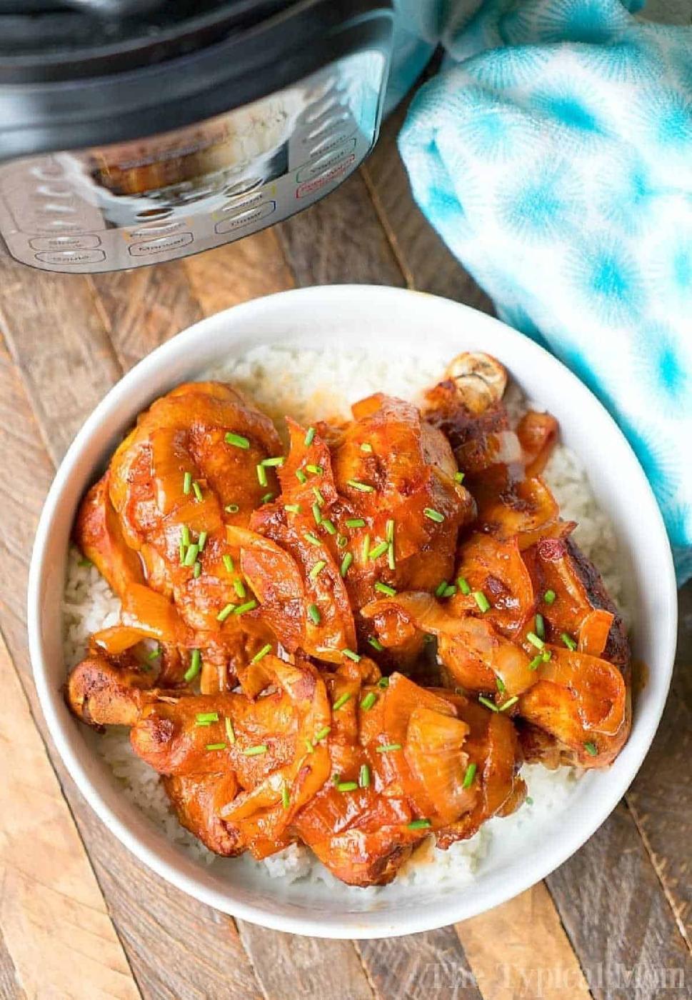 A bowl of rice topped with saucy instant pot chicken legs and chopped chives sits next to an electric pressure cooker.