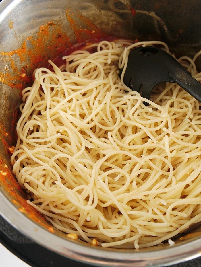 Spaghetti in a pot with tomato sauce remnants and a black pasta serving spoon, reminiscent of a quick instant pot chicken parmesan evening delight.
