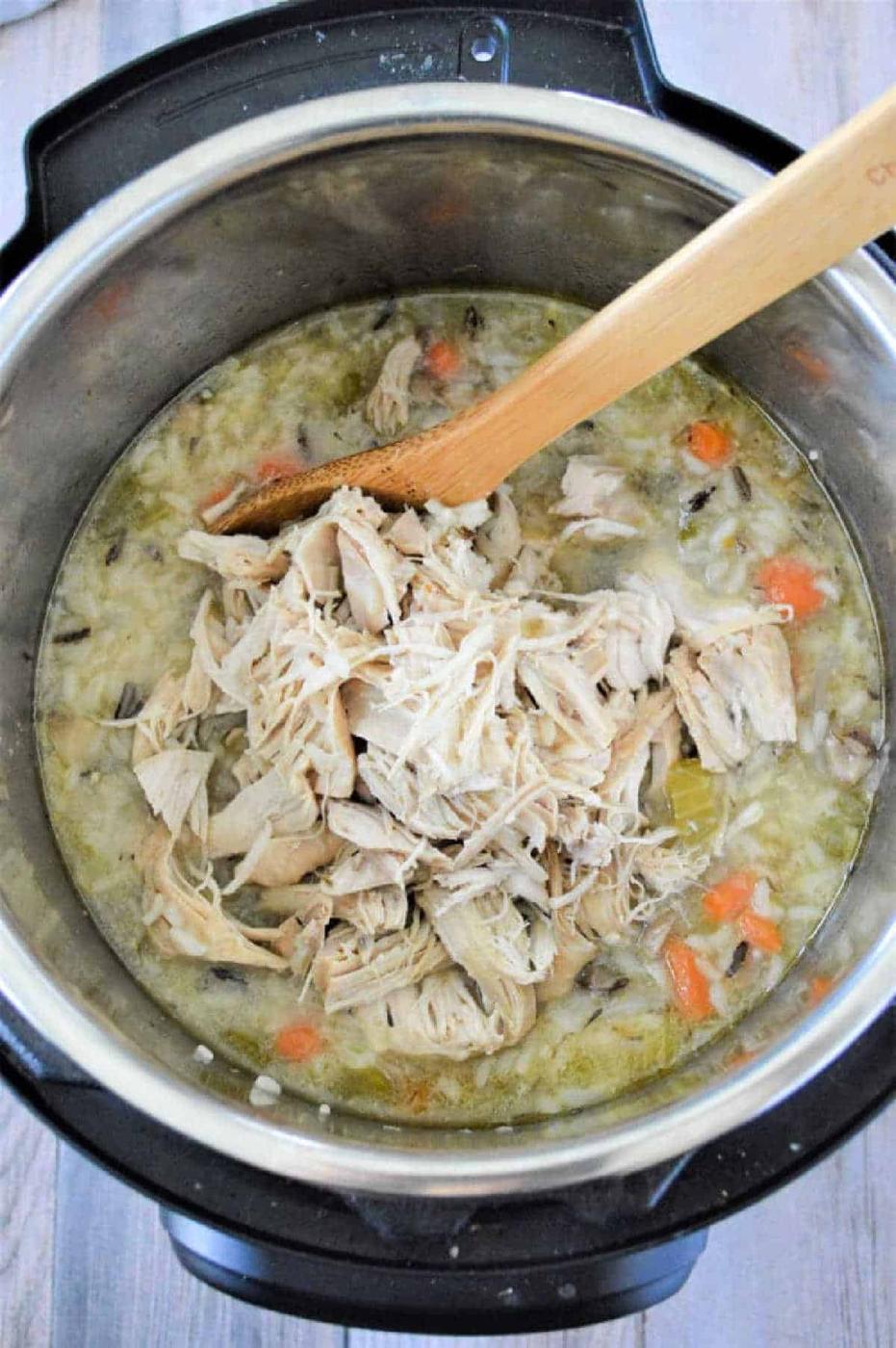 Shredded chicken, vegetables, and rice simmer together in this flavorful instant pot chicken rice soup, all stirred gently with a wooden spoon.