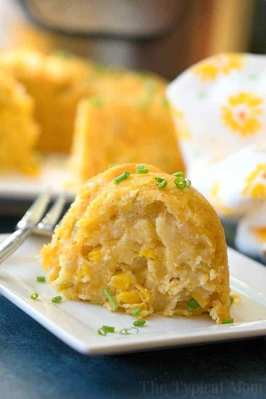 A slice of cornbread with corn kernels, inspired by an instant pot corn casserole recipe, topped with chopped chives, on a white plate with a fork.