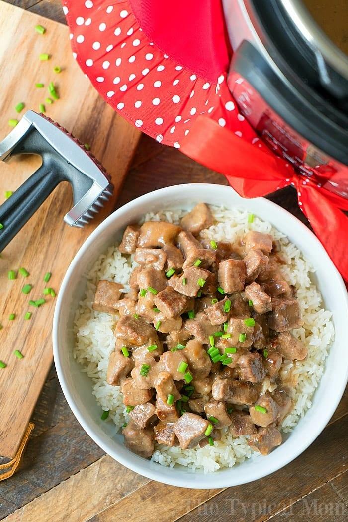A bowl of savory beef steak with rice, garnished with chives, sits invitingly next to a meat tenderizer and an Instant Pot—perfect for when youre craving that cube steak tenderness.
