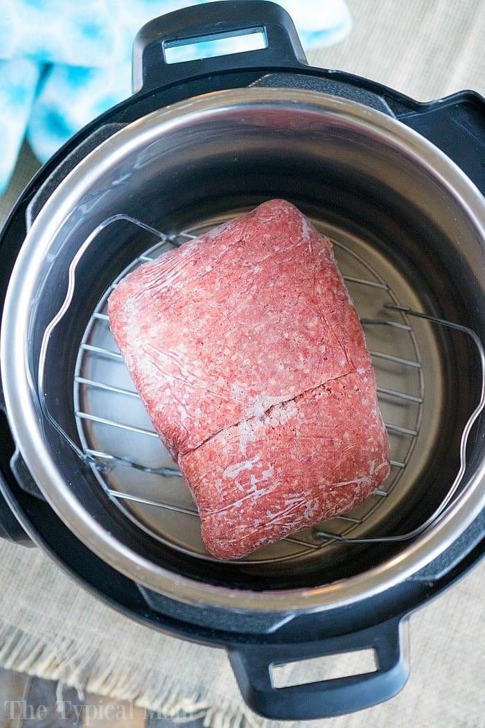 A block of instant pot frozen ground beef sits on a metal trivet inside the pressure cooker, ready to be cooked quickly and easily.