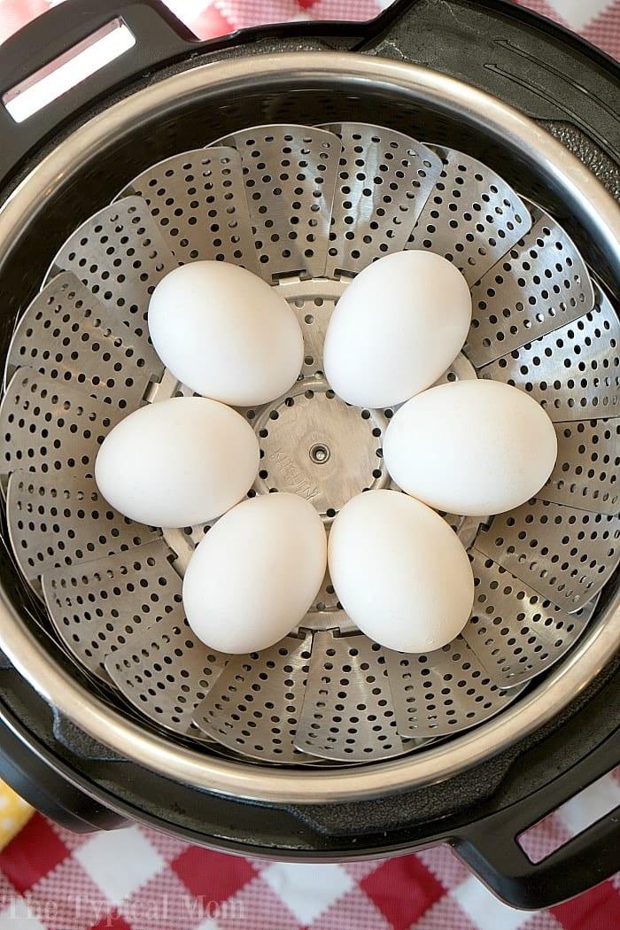 Six white eggs rest on a metal steamer basket inside an Instant Pot, ready to be transformed into an easy instant pot potato salad.