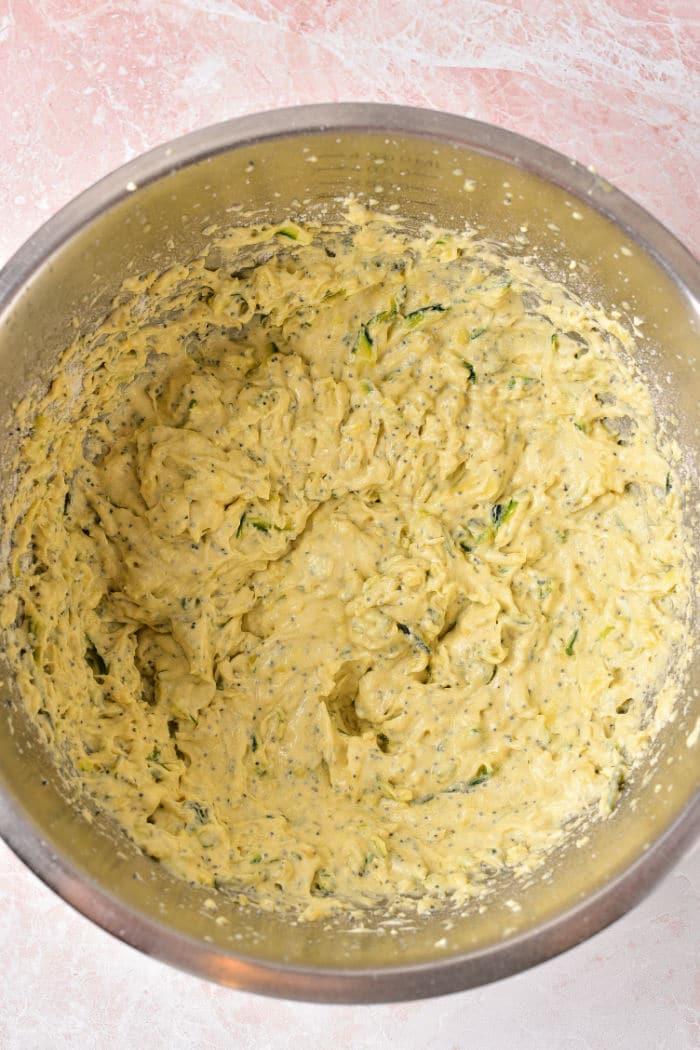 A mixing bowl filled with lemon poppy seed bread batter sits invitingly on a pink countertop, reminiscent of preparing an instant pot lemon poppy seed cake.