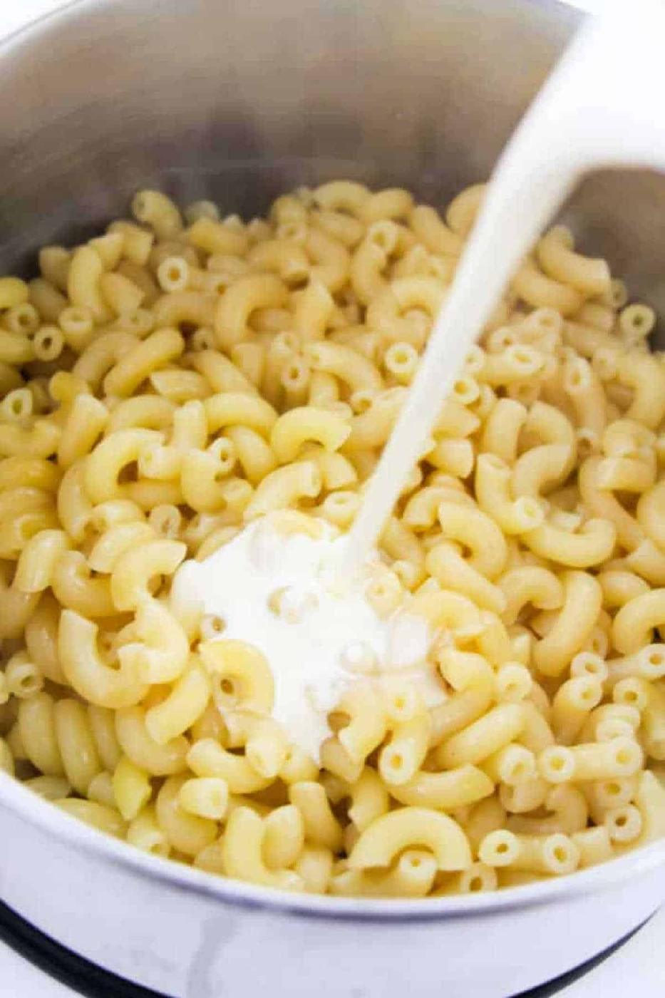 A pot of cooked instant pot macaroni and cheese with milk being poured over it, ready for mixing.