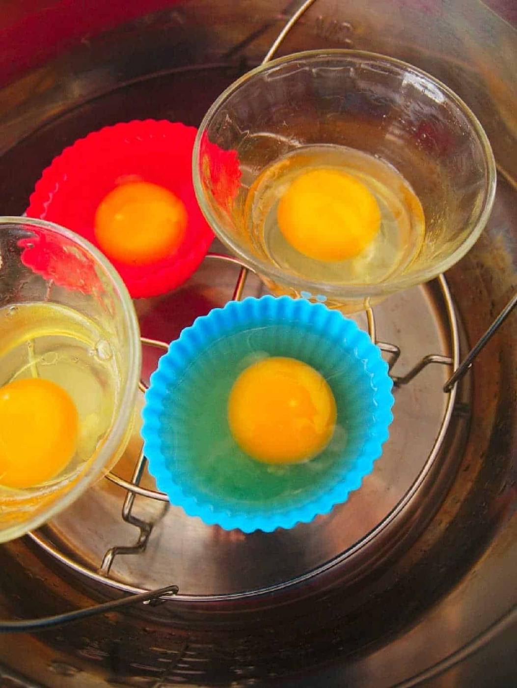 Eggs cracked into glass bowls and silicone cups, ready for steaming in a metal pot, steamer, or for making instant pot poached eggs.