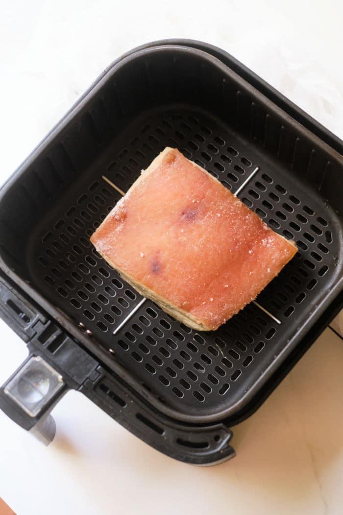 A slice of pork belly being toasted inside an air fryer basket pairs perfectly with the savory flavors of instant pot pork belly.