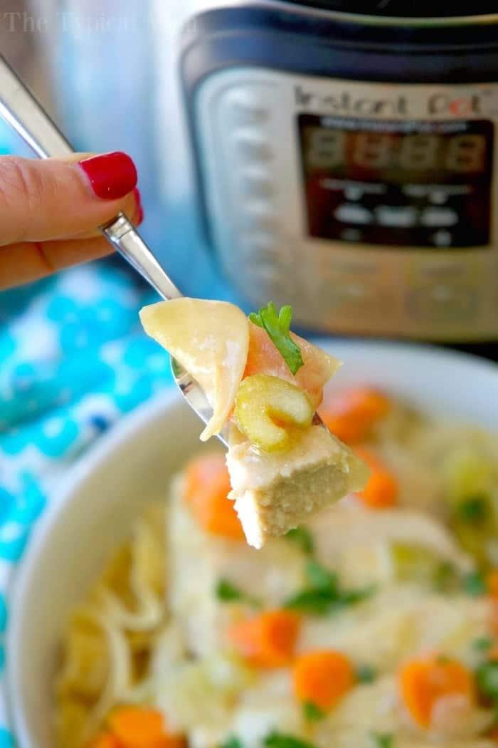 A fork holds chicken, noodles, and carrots above a bowl, with an Instant Pot in the background—perfect for trying your favorite instant pot pork stroganoff recipe.