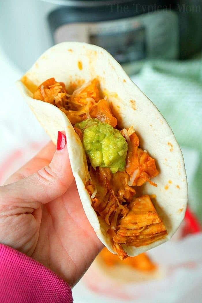 A hand holds a taco filled with guacamole and savory instant pot shredded chicken, offering a delicious bite.