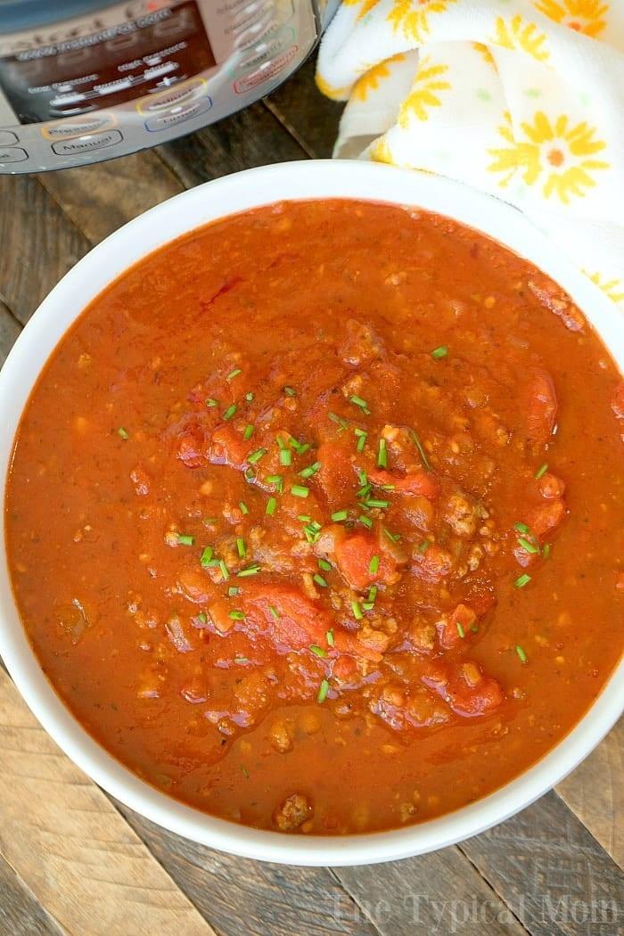 A bowl of hearty spaghetti sauce garnished with herbs sits next to an Instant Pot, ready to whip up a delicious spaghetti sauce, all on a rustic wooden surface.
