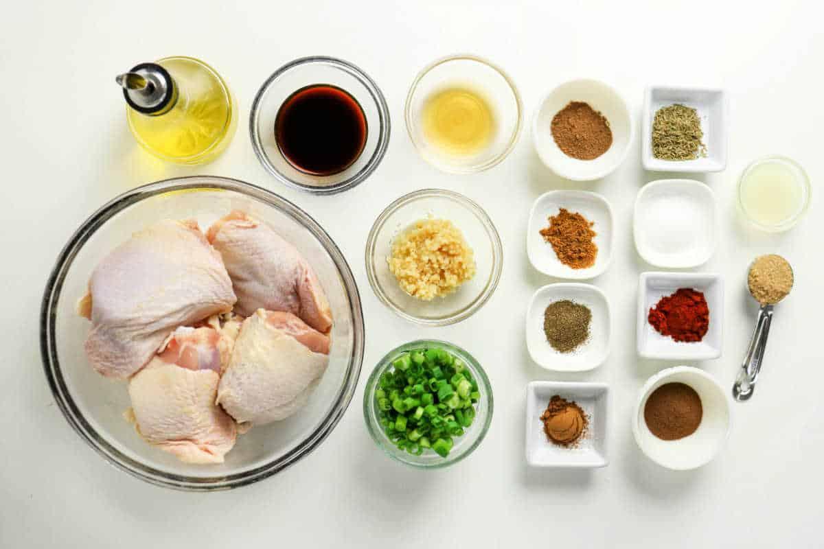 Raw chicken thighs, chopped green onions, minced garlic, sauces, oil, and various spices arranged on a white surface—perfect for preparing flavorful Oven Jerk Chicken.