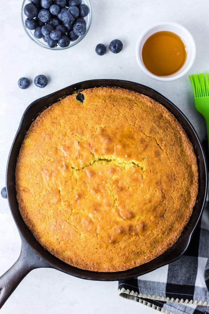 Jiffy cornbread in a cast iron skillet, served with fresh blueberries and a drizzle of honey on the side.