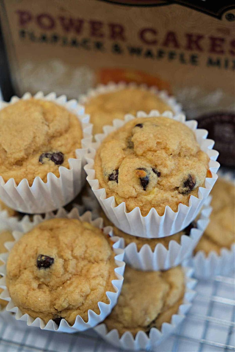 A stack of Kodiak Muffins in white paper liners sits in front of a box of pancake mix, tempting you with every chocolate chip.