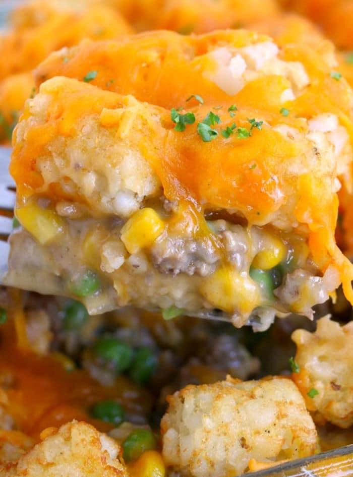 Close-up of cheesy tater tot casserole with ground beef, corn, peas, and melted cheddar on a spatula—a tasty twist for those seeking creative leftover meatloaf recipes.
