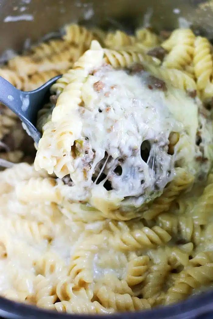 A spoon scoops cheesy, creamy rotini pasta with melted cheese and savory ground meat—perfect for those craving creative leftover meatloaf recipes.