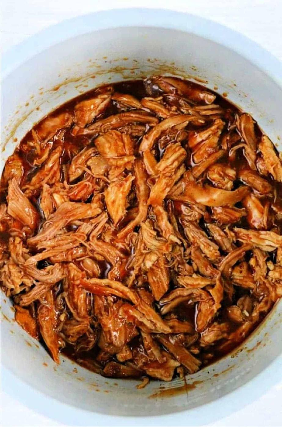Shredded barbecue pork in a white pot, covered in rich, dark sauce, reminiscent of those delicious leftover pork loin recipes.