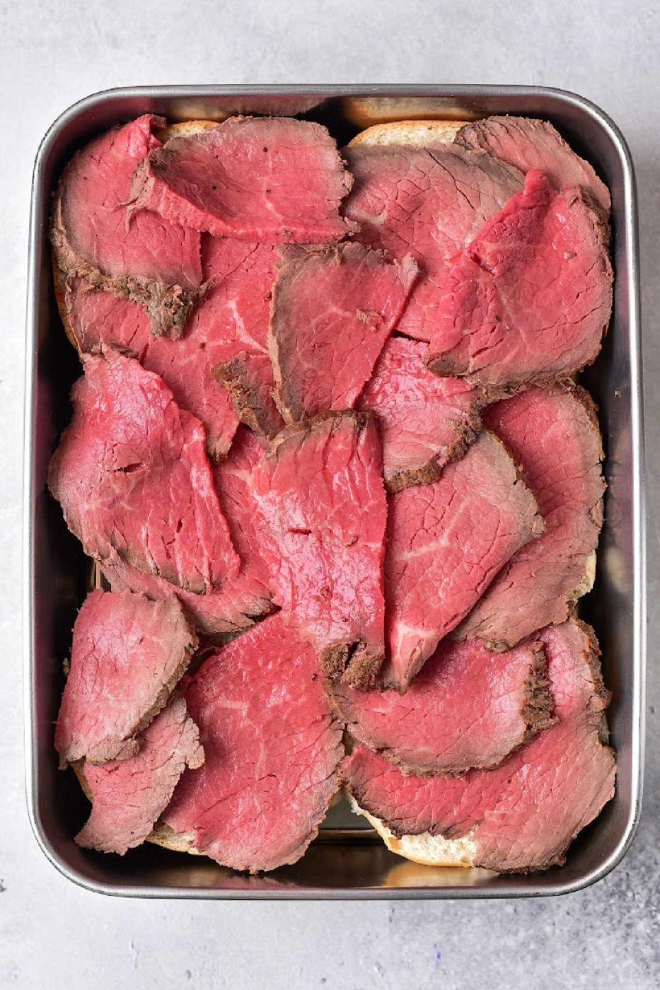 Slices of rare beef, perfect for leftover tri tip recipes, are arranged in a metal tray on a gray background.