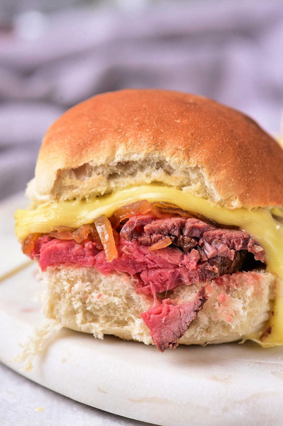 Close-up of a sandwich crafted from leftover tri-tip, complemented by melted cheese and grilled onions nestled in a fresh bun.