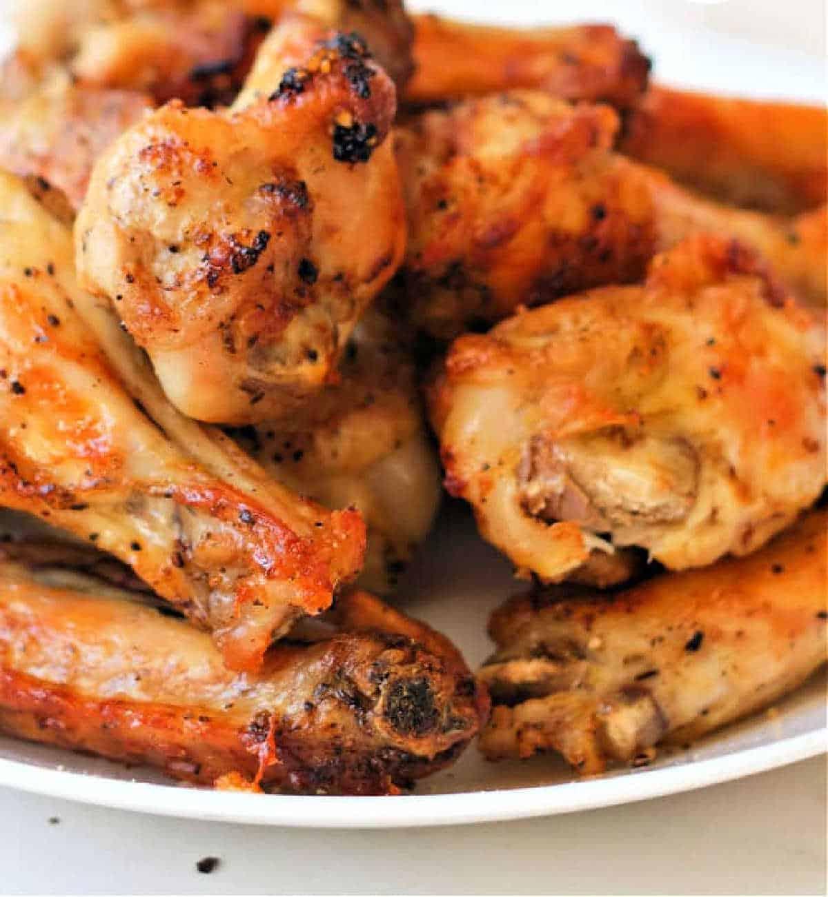 A close-up image of a plate filled with lemon pepper chicken wings, cooked to perfection in an air fryer. The wings boast a slightly charred and seasoned exterior, with a golden-brown color that adds to their appeal. The white plate enhances the presentation of this delectable dish.