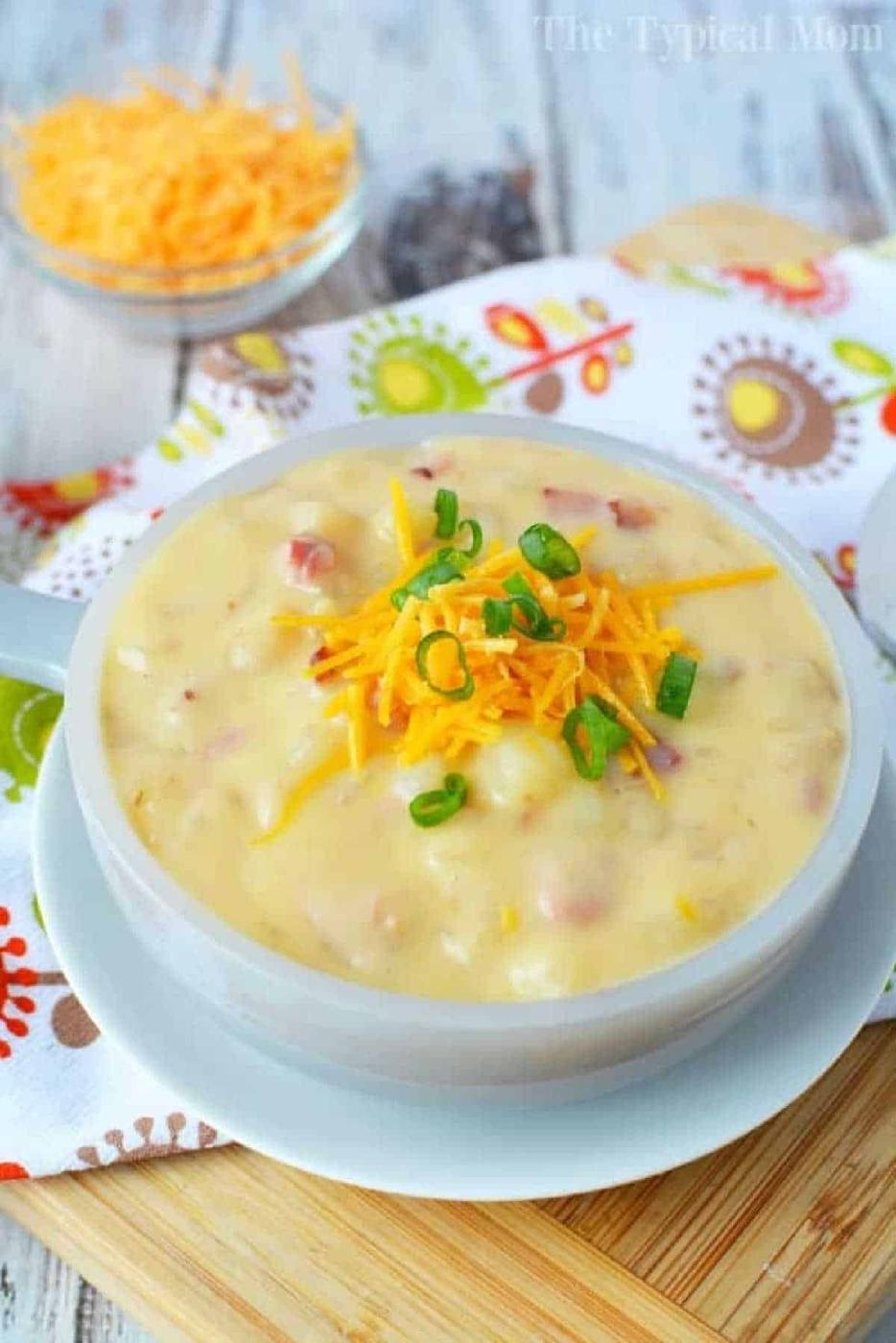 A bowl of creamy Crockpot loaded baked potato soup topped with shredded cheese and chopped green onions.