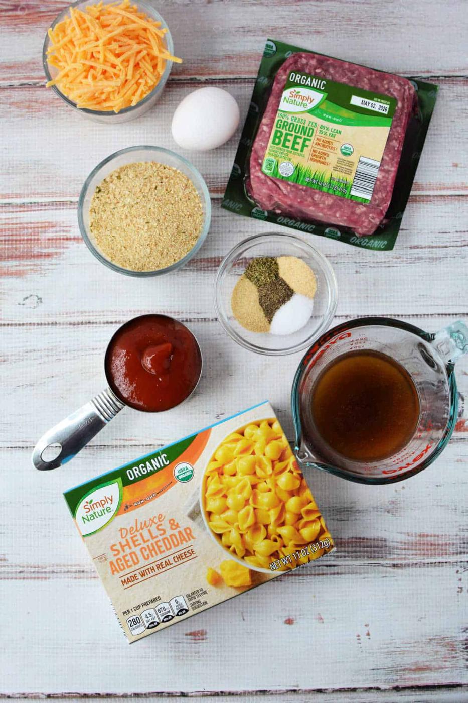 Ingredients for a cheesy casserole, blending pasta, ground beef, cheese, egg, broth, sauce, and seasonings—like a tasty mash-up of cheeseburger and classic mac and cheese.