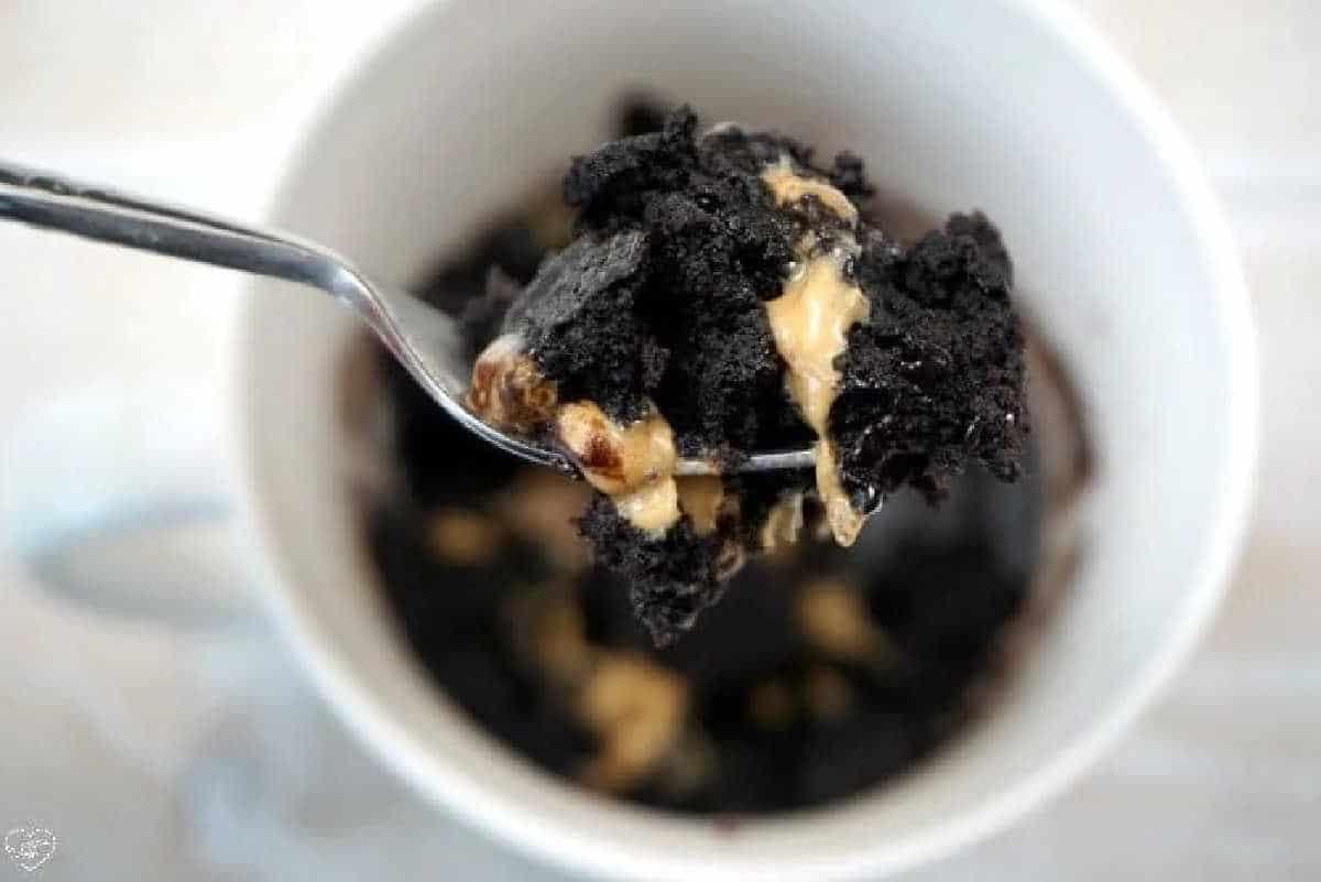 Spoonful of chocolate cake and peanut butter being lifted from a white mug, showing just how easy it is to make a brownie in a mug for a quick, delicious treat.