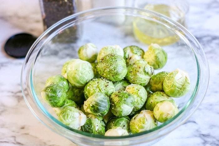 A glass bowl filled with Brussels sprouts sits elegantly on a marble countertop.