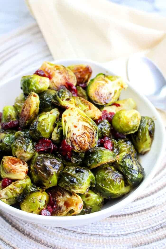 A bowl of Brussels sprouts with cranberries sits on the table, accompanied by a spoon, offering a delightful taste. Discover the ease of preparation by learning how to microwave Brussels sprouts for a quick and delicious alternative.