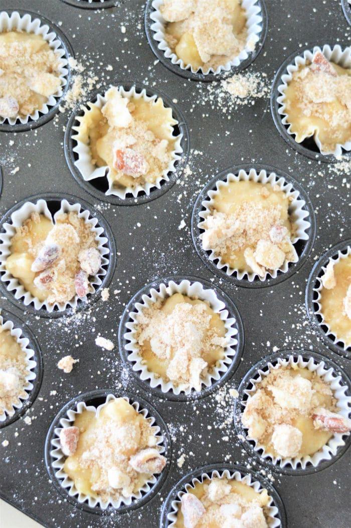 A muffin tray brimming with batter for mini muffins, crowned with streusel toppings, ready to bake.