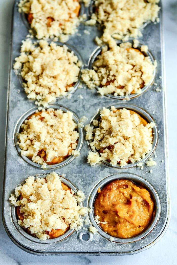 Muffin tin with unbaked mini pumpkin muffins, some topped with crumbly streusel, ready to go in the oven.