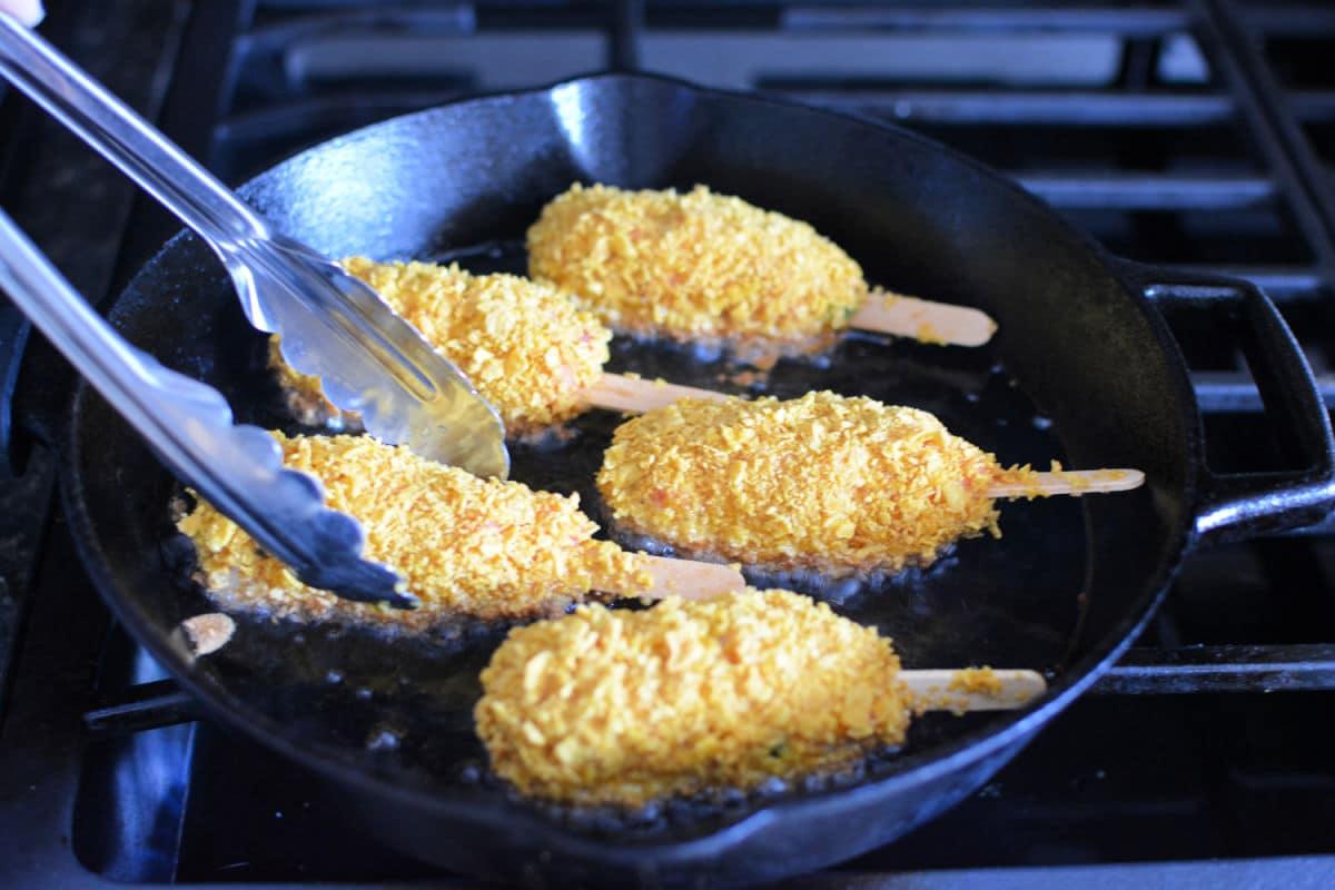 Four mock chicken legs frying in a cast iron skillet