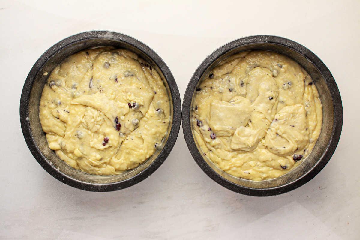 Two round baking pans filled with raw muffin mix batter, speckled with blueberries, to make a cake