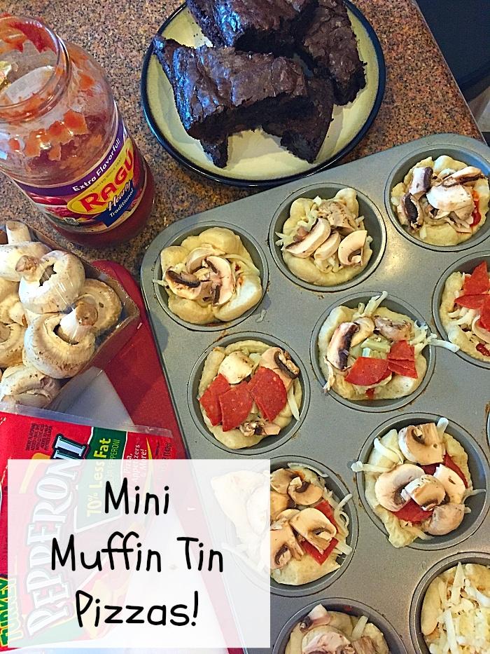 A tray of uncooked mini muffin tin pizzas awaits, topped with mushrooms and pepperoni, showcasing a delightful muffin tin dinner idea. A jar of pasta sauce and a box of pepperoni sit nearby. In the background, dark-colored baked items rest on a plate. Label reads Mini Muffin Tin Pizzas!