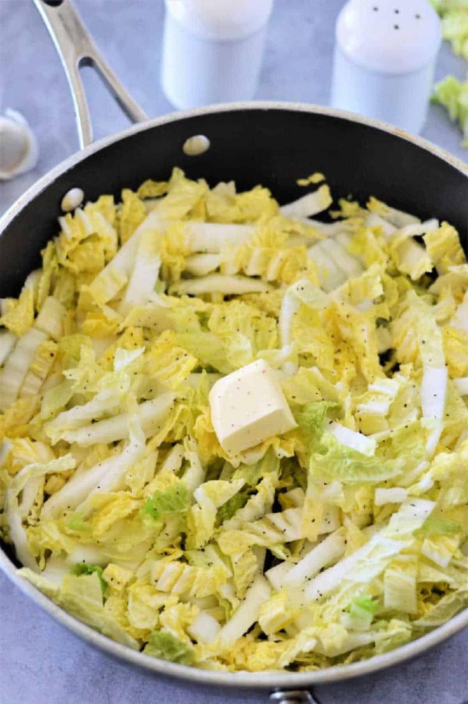 Chopped Napa cabbage with a pat of butter and black pepper in a skillet, ready to be cooked—an easy and delicious Napa cabbage recipe.