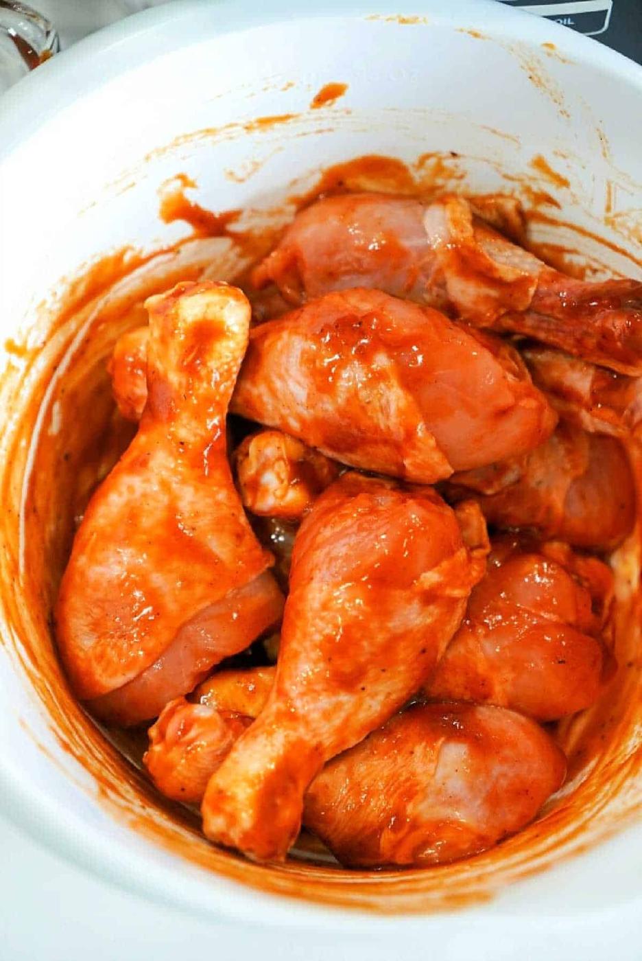Raw chicken drumsticks coated in a red marinade sit enticingly inside a white bowl, ready to be transformed into a delicious meal with the Ninja Foodi.