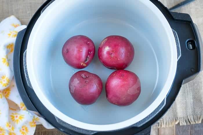Four red potatoes sit inside an empty electric pressure cooker on a wooden surface, ready to be paired with Ninja Foodi corned beef and cabbage for a hearty meal.