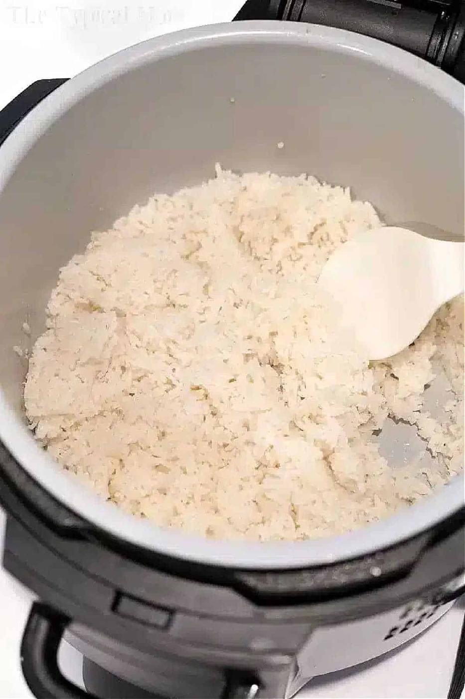 Cooked white rice being stirred with a spoon inside a Ninja Foodi rice cooker.