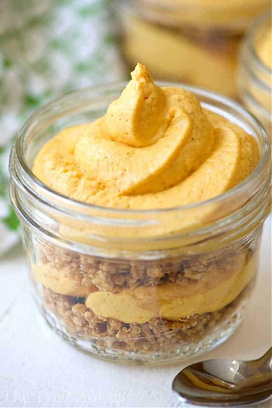 A glass jar with layers of crumbled crust and creamy pumpkin mousse, topped with a swirl of mousse—this No Bake Pumpkin Cheesecake in Jars is the perfect easy, festive treat.