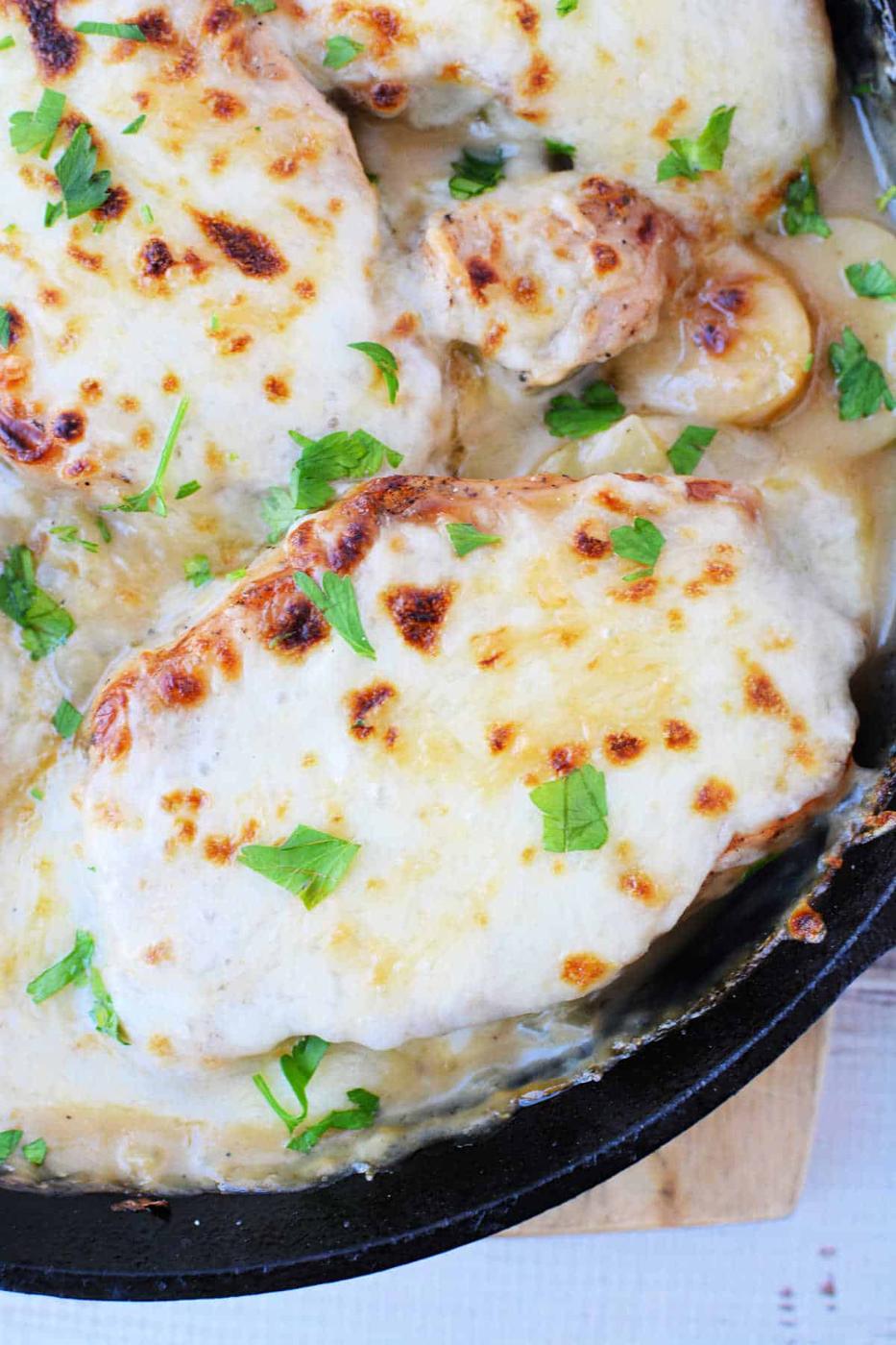 Chicken breasts in a creamy sauce, topped with melted cheese and fresh parsley in a skillet—try this technique with oven baked pork chops or pork chops with potatoes for a hearty twist.