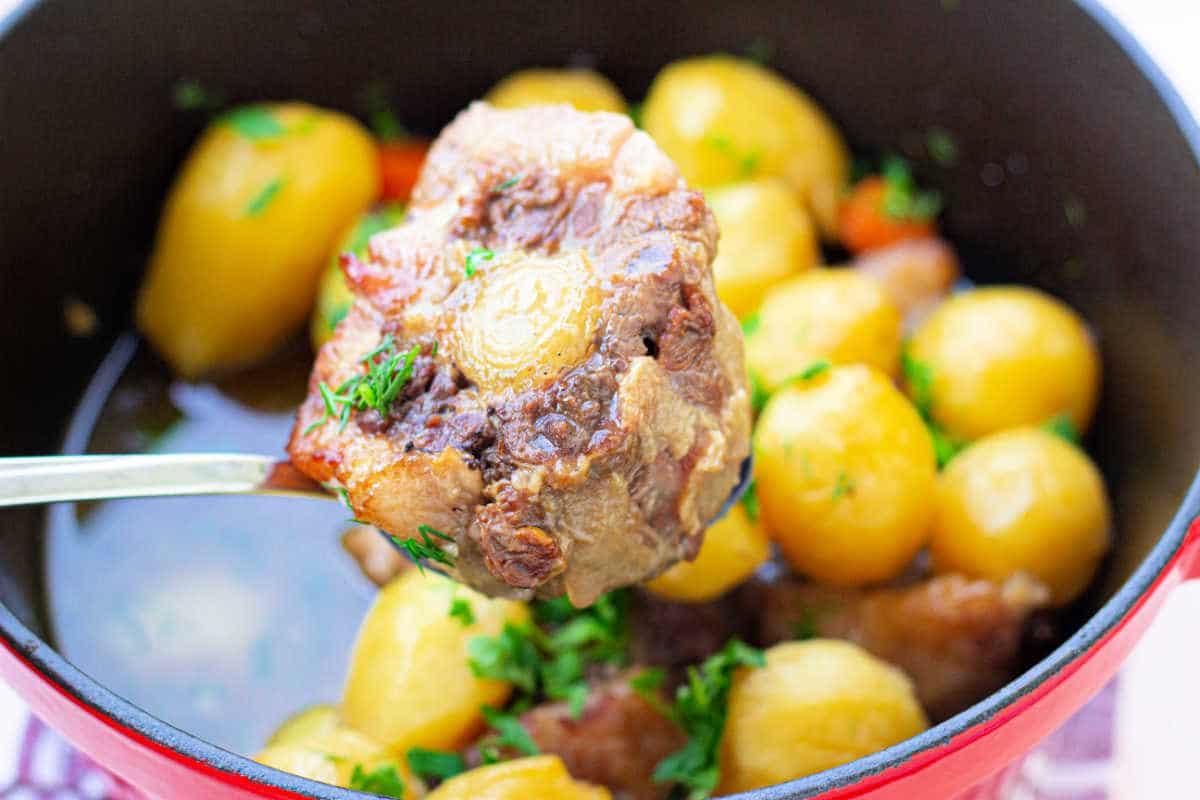 Close-up of a spoon lifting ox beef stew with potatoes and carrots from the pot, reminiscent of a hearty ox tail soup, garnished with parsley.