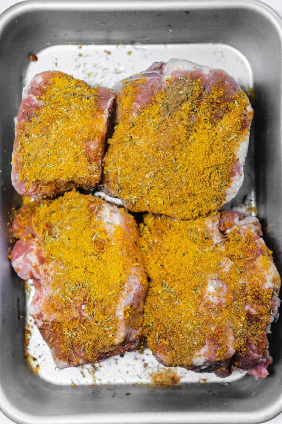 Four raw pieces of meat in a metal tray, coated with a yellow spice rub—perfect for preparing a flavorful Oxtail Curry.