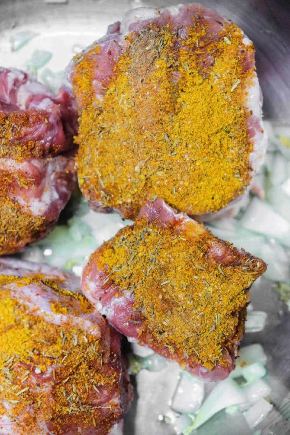Raw oxtail pieces topped with a vibrant yellow spice blend, set on a bed of chopped onions in a metal pan, ready to be transformed into flavorful Oxtail Curry.