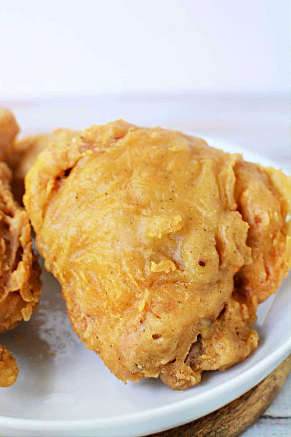 A piece of golden, crispy Pan Fried Chicken thighs sits on a white plate, ready to enjoy.